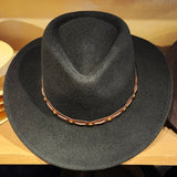 A black felt cowboy hat with a brown band decorated with small gold-colored studs, displayed on a wooden shelf.