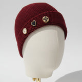 Maroon knit beanie with decorative buttons on a mannequin head against a gray background