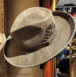 A Western inspired Shantung Straw fedora hat hand dyed in a warm grey brown wash featuring embossed leather and feathers
