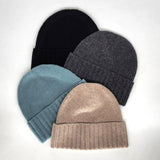 Four knit beanie hats in black, gray, blue, and beige on a light gray background