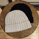 Two knit hats, one beige and one black, on a wooden surface.